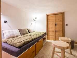 Une chambre à coucher avec un lit, une armoire en bois, un petit tabouret et une lampe fixée au mur.