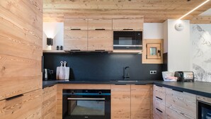 Uma cozinha moderna com armários de madeira, bancada preta, forno embutido e micro-ondas.