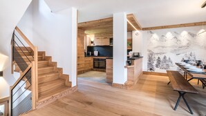 Interior moderno com escada de madeira, cozinha com armários de madeira e área de jantar com mesa de madeira.