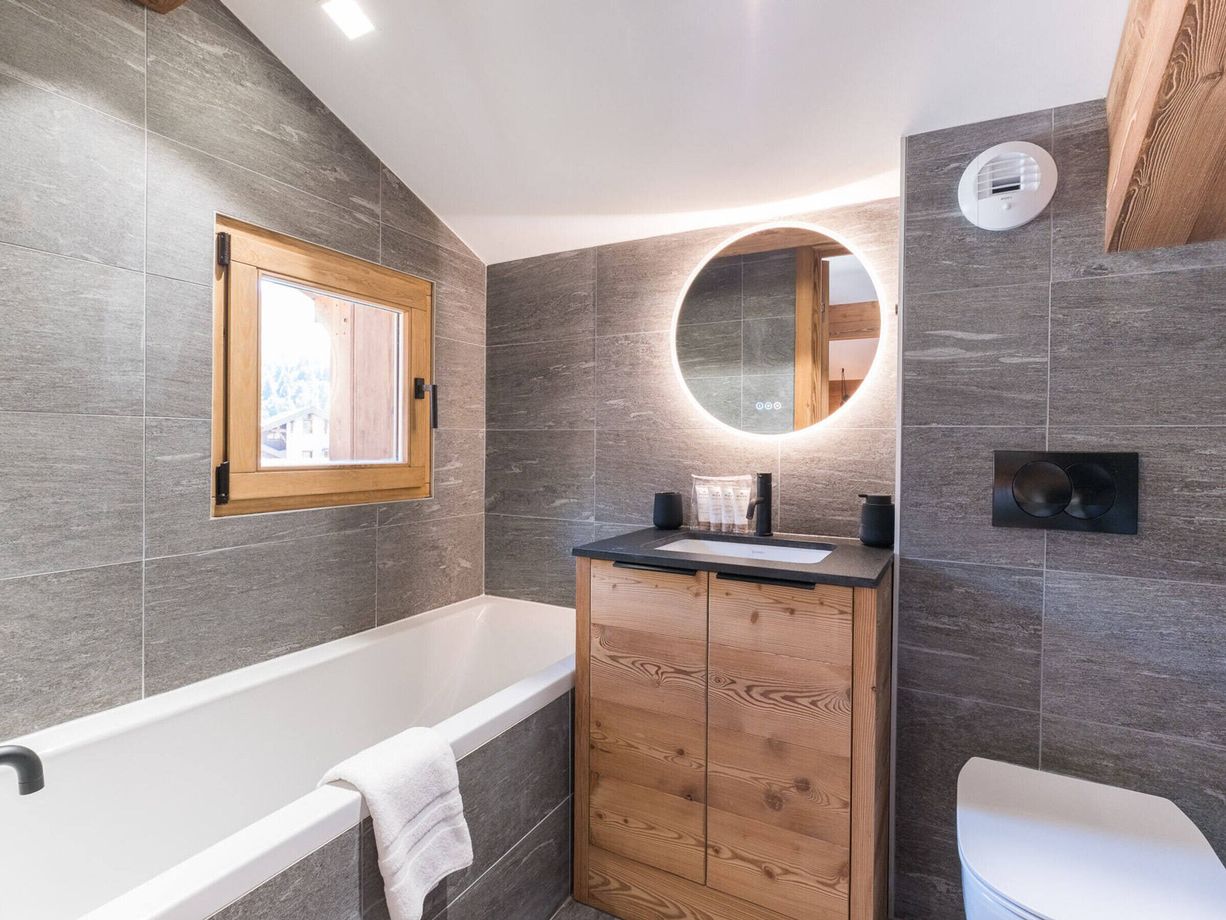 Une salle de bain moderne avec une baignoire, un meuble-lavabo en bois et un miroir rond.