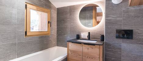 Une salle de bain moderne avec une baignoire, un meuble-lavabo en bois et un miroir rond.