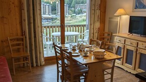 Ein Essbereich mit Holztisch und Stühlen, einem Fernseher und Blick auf Gebäude durch große Fenster.