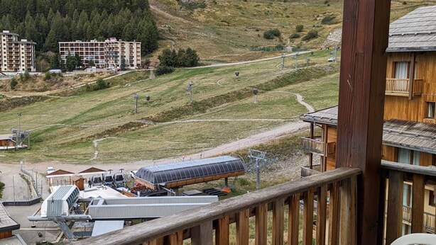 Ein Holzhaus mit Balkon, das auf eine hügelige Landschaft mit einer Straße und einer Solaranlage blickt.