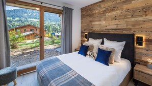 Un dormitorio con una cama grande, cabecera de madera, mesita de noche y vistas a un paisaje montañoso a través de un ventanal corredera.