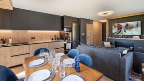 Una cocina moderna con armarios oscuros, una mesa de comedor de madera con platos y vasos, y un televisor de pantalla plana grande montado sobre una chimenea.