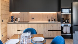 Una cocina moderna con armarios oscuros, encimera de madera y comedor con sillas azules y mesa preparada para cuatro personas.