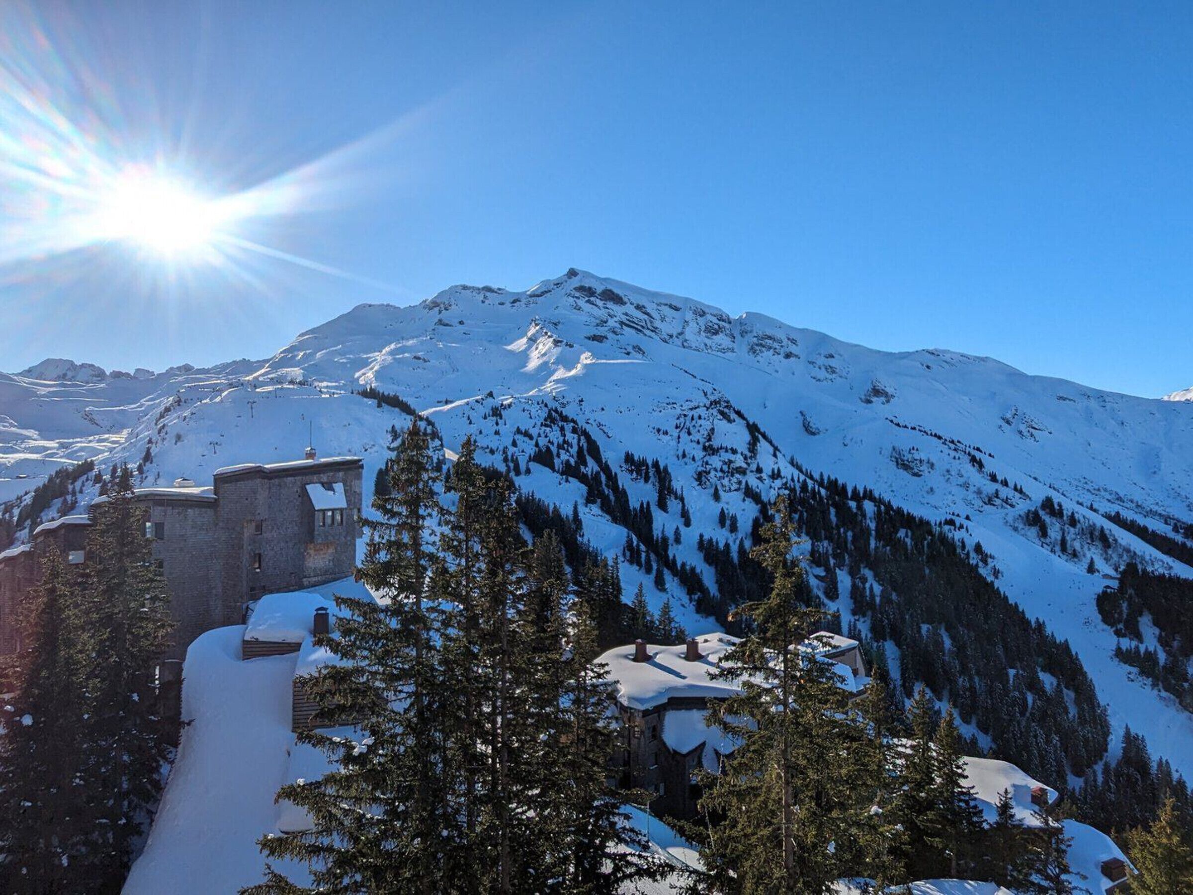 A snow-covered mountain with a clear sky and a building with a snow-covered roof.