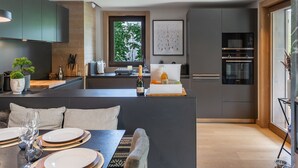 Een moderne keuken met donkere kastjes, een centraal eiland en een eetgedeelte met een tafel voor vier personen.