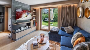 Een moderne woonkamer met een grote televisie, een blauwe bank en een glazen salontafel.