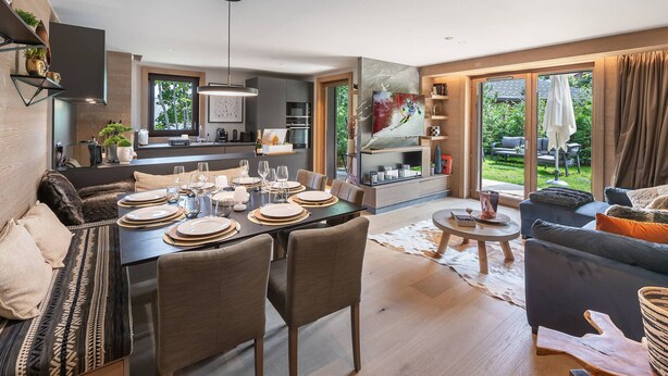 Een moderne, open woonkamer met een eettafel gedekt voor een maaltijd, een bank en een aan de muur bevestigde televisie.