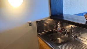Cozinha moderna com pia de aço inoxidável, armários de madeira e luminária fixa na parede.