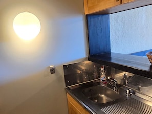 Une cuisine moderne dotée d’un évier en acier inoxydable, de meubles en bois et d’un luminaire fixé au mur.