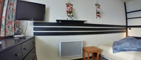 Una habitación compacta con cama, un taburete de madera, televisión y un calentador instalado en la pared.