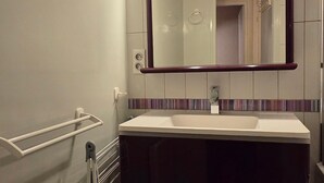 Casa de banho com lavatório branco, espelho com moldura de madeira e porta-toalhas.