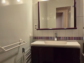 Une salle de bain avec un lavabo blanc, un miroir avec un cadre en bois et un porte-serviettes.