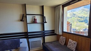 Quarto com cama, janela com vista para uma paisagem montanhosa e prateleira com objeto decorativo.