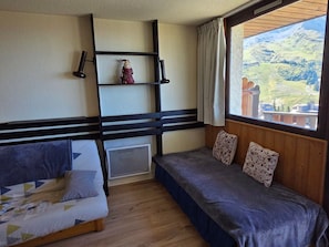 Une chambre avec un lit, une fenêtre donnant sur un paysage montagneux et une étagère ornée d’un objet décoratif.