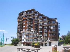 Um hotel com vários andares, varandas e uma estação de esqui ao fundo.