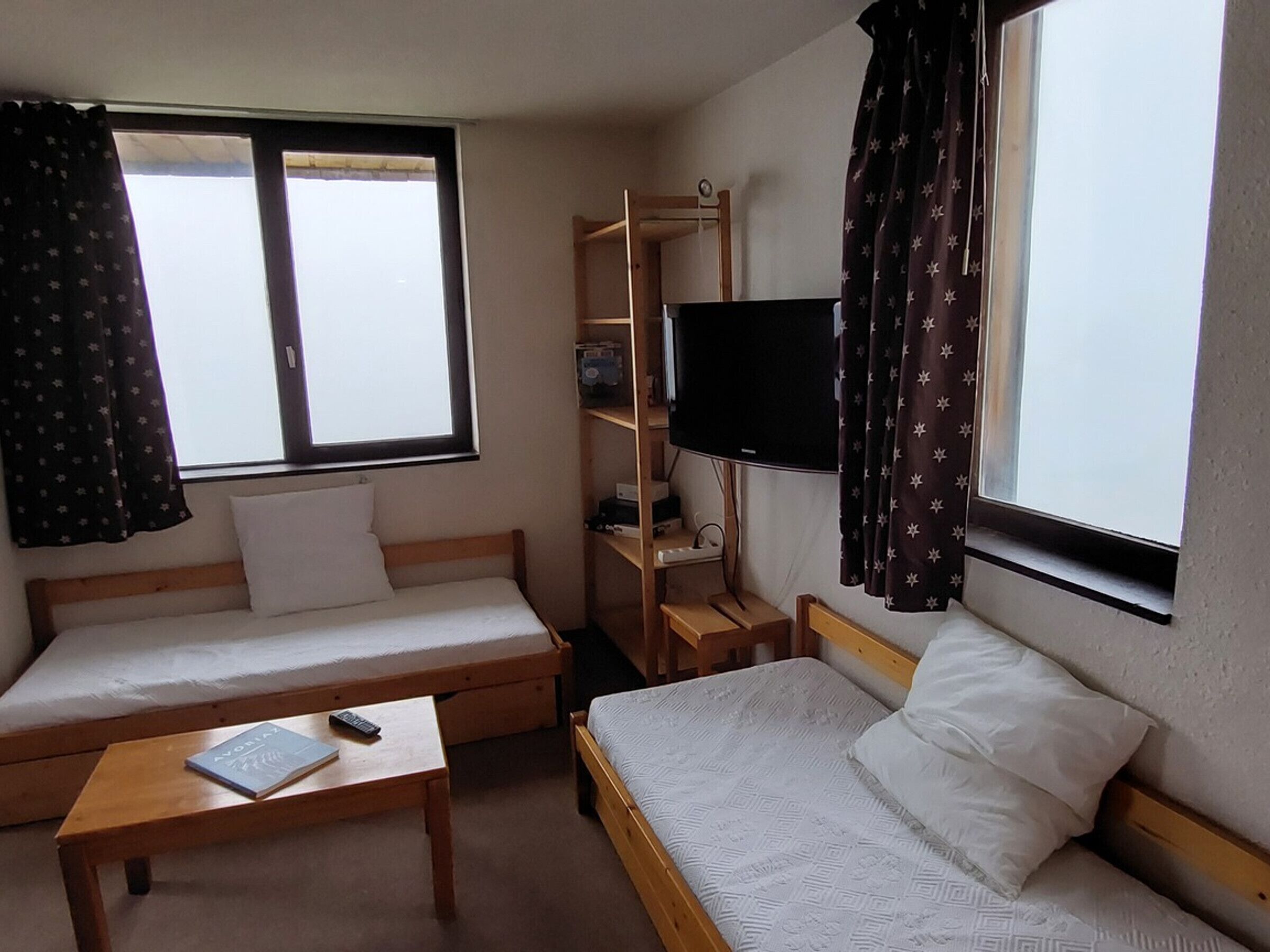 A room with two beds, a small table, a TV, and a window with curtains.