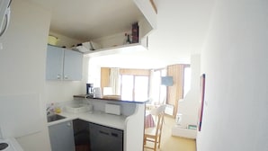 A compact kitchen with a sink, a small refrigerator, and a microwave. There is a dining area with a chair and a table.