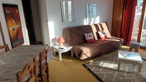 A cozy living room with a sofa, a small table with a lamp, a patterned rug, and a dining area with chairs.