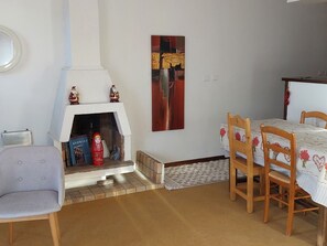 Uma sala de estar com lareira, uma mesa de jantar com cadeiras e uma poltrona pequena.