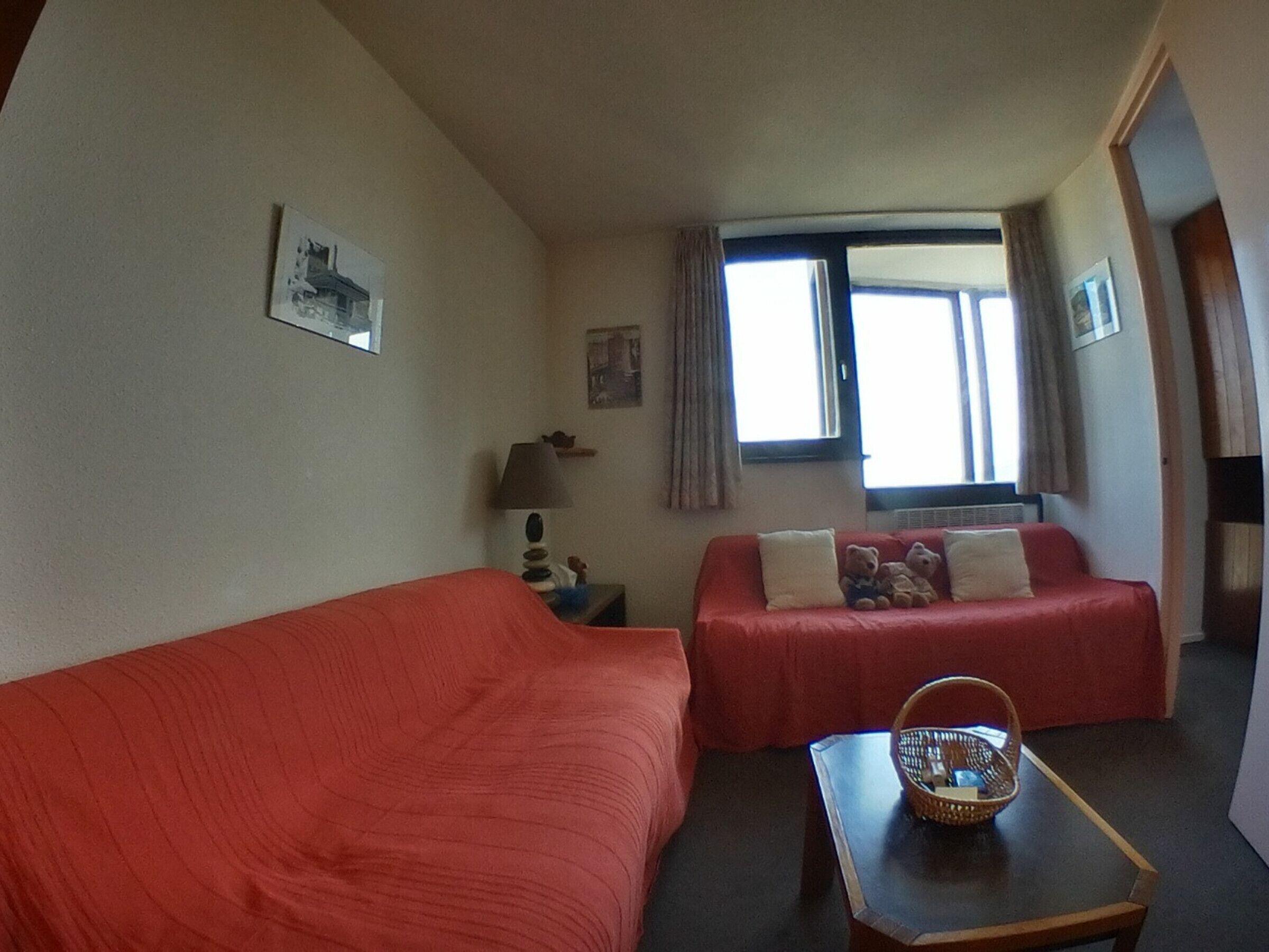 Een kamer met twee eenpersoonsbedden, een tafeltje met een mand, een lamp en een raam met gordijnen.