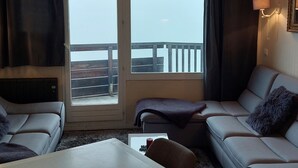 Et hotelværelse med balkon, sofa, stol, lille bord og lampe.