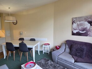 A modern living room with a grey sofa, a dining table with chairs, a small side table, and a large floral artwork on the wall.
