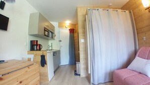A compact room with a kitchenette, a wooden desk, a bed, and a shower curtain. - Renovated Studio for 4, balcony, ski-in/ski-out (Avoriaz)