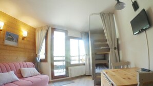 A cozy room with a pink sofa, a wooden desk, and a TV mounted on the wall. - Renovated Studio for 4, balcony, ski-in/ski-out (Avoriaz)
