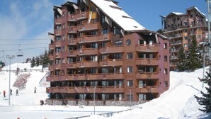 A multi-story hotel with balconies, ski lift in the background, and snow on the ground.