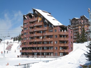 Um hotel com vários andares e varandas, um teleférico ao fundo e neve no chão.