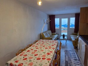 Un rincón comedor acogedor con una mesa dispuesta para dos, un sofá y vistas a las montañas a través de un ventanal.