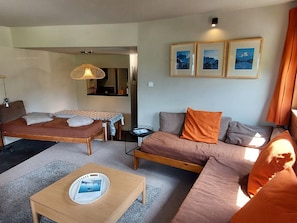Um espaço de estar compacto com cama, sofá e uma pequena mesa. Há quadros nas paredes e um lustre pendurado.