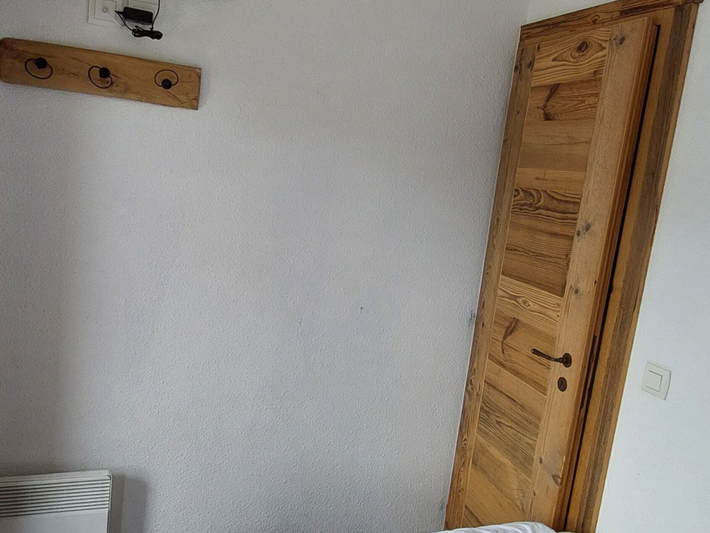 A room with a wooden wardrobe, a white radiator, and a wooden shelf with three circular hooks.
