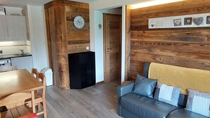 A compact living space with a wooden accent wall, a sofa, a dining table, and a kitchen area. - Charming 2-Room Cabin for 6 in Avoriaz Center (Avoriaz)
