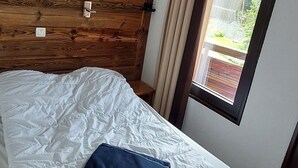 A bedroom with a wooden headboard, a white bedspread, and a window with curtains. - Charming 2-Room Cabin for 6 in Avoriaz Center (Avoriaz)