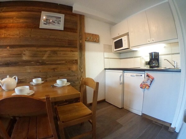Une cuisine compacte avec un mur d’accent en bois, un four à micro-ondes, une machine à café et un petit réfrigérateur.
