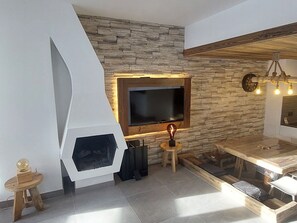 Uma sala de estar moderna com parede de pedra, lareira, televisão e mesa de jantar de madeira.