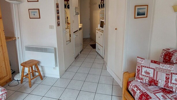 A narrow hallway with a wooden stool, a white radiator, and a red and white patterned sofa.
