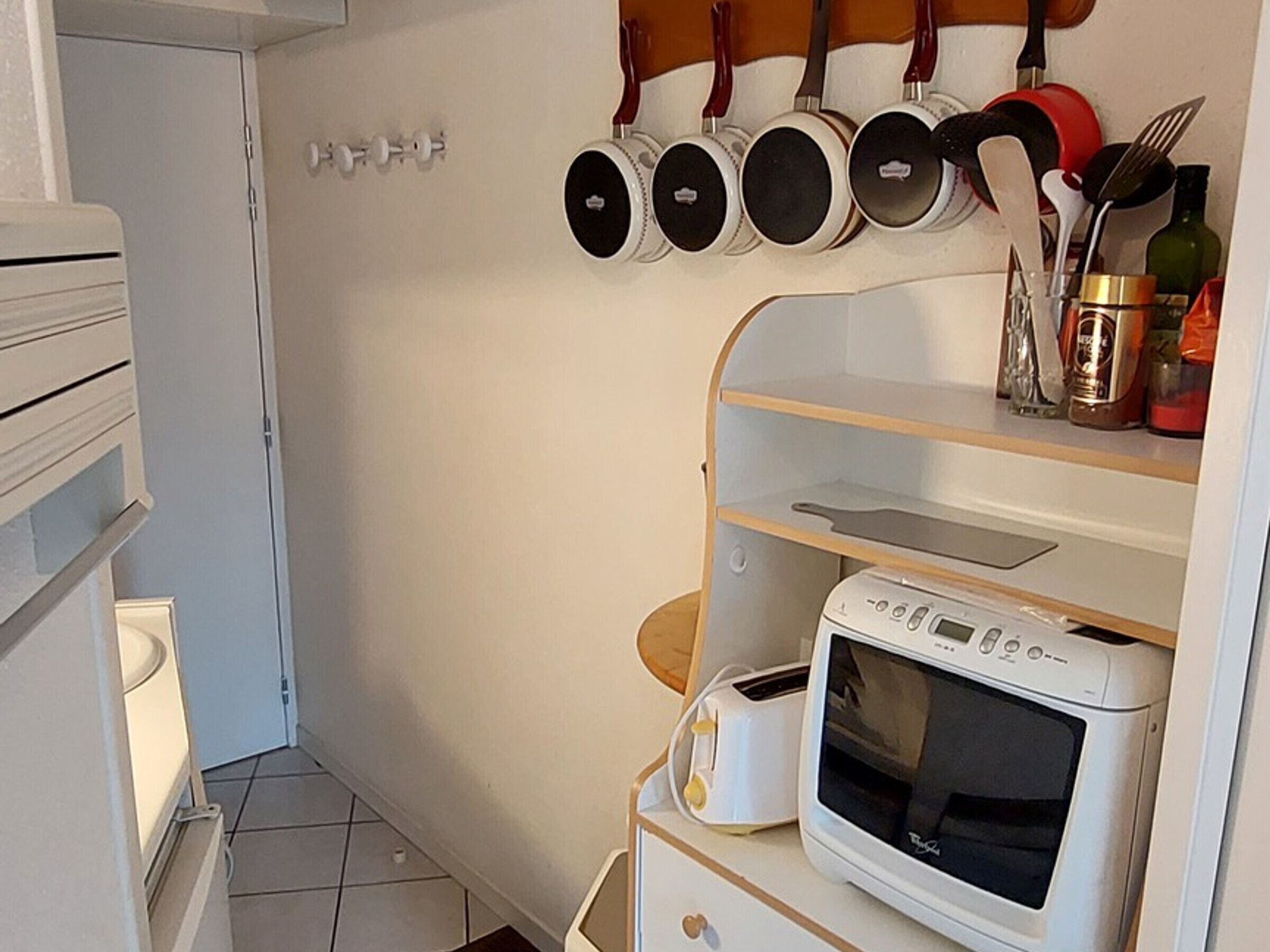A kitchen with a microwave, toaster, and a shelf with pots and pans.