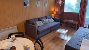 A cozy room with a sofa, a small table with a teapot and cups, a lamp, and a bed.
