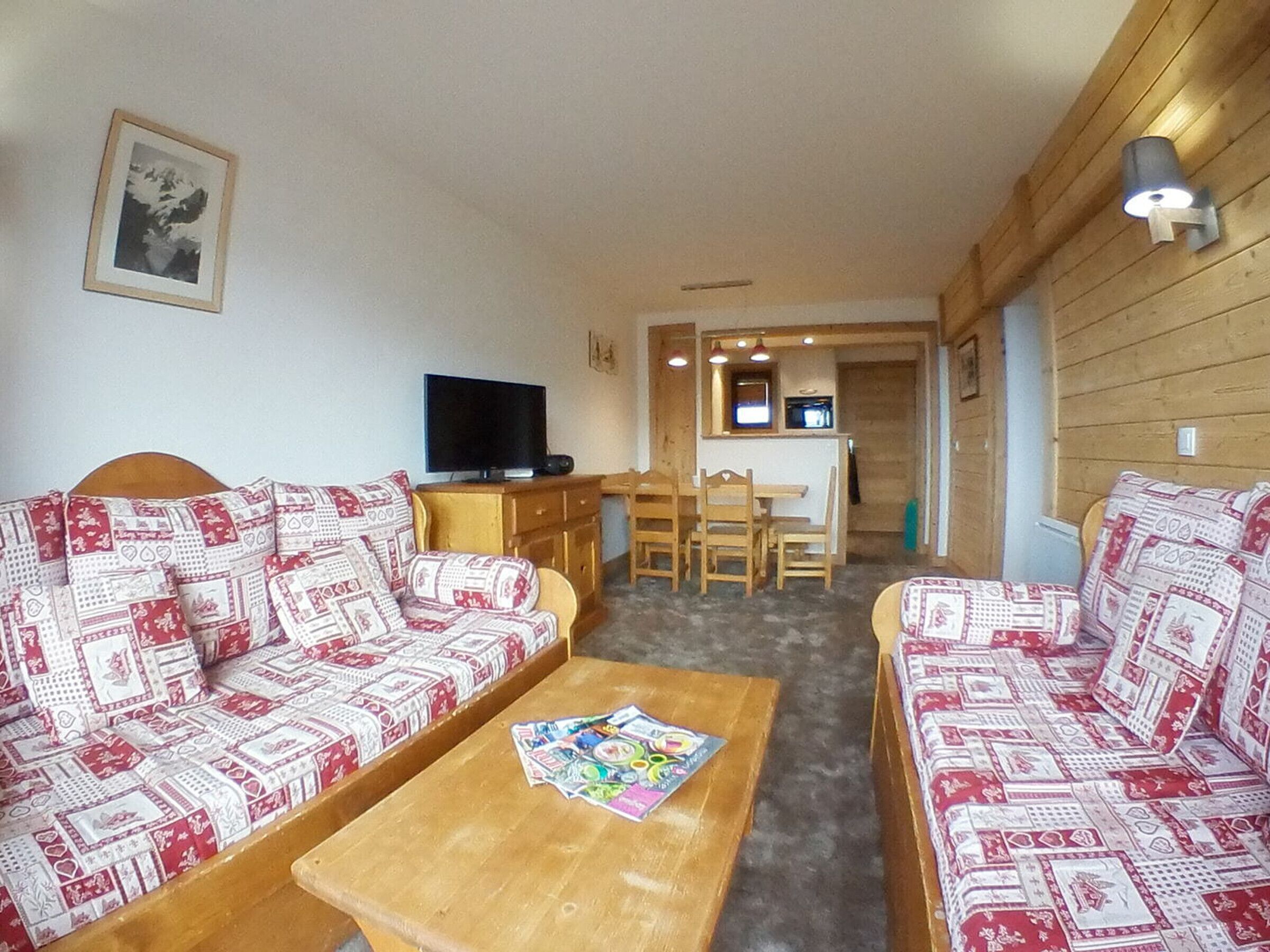 Una sala de estar acogedora con sofás estampados, una mesa de centro de madera y un televisor.