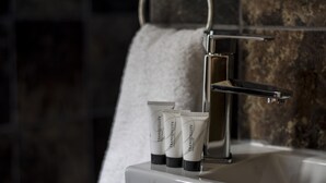 Un baño con un lavamanos blanco, tres tubos de loción y una toalla colgada en un perchero.