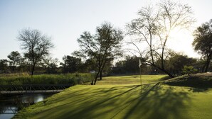 Campo de golf con un cuerpo de agua, árboles y un puente.