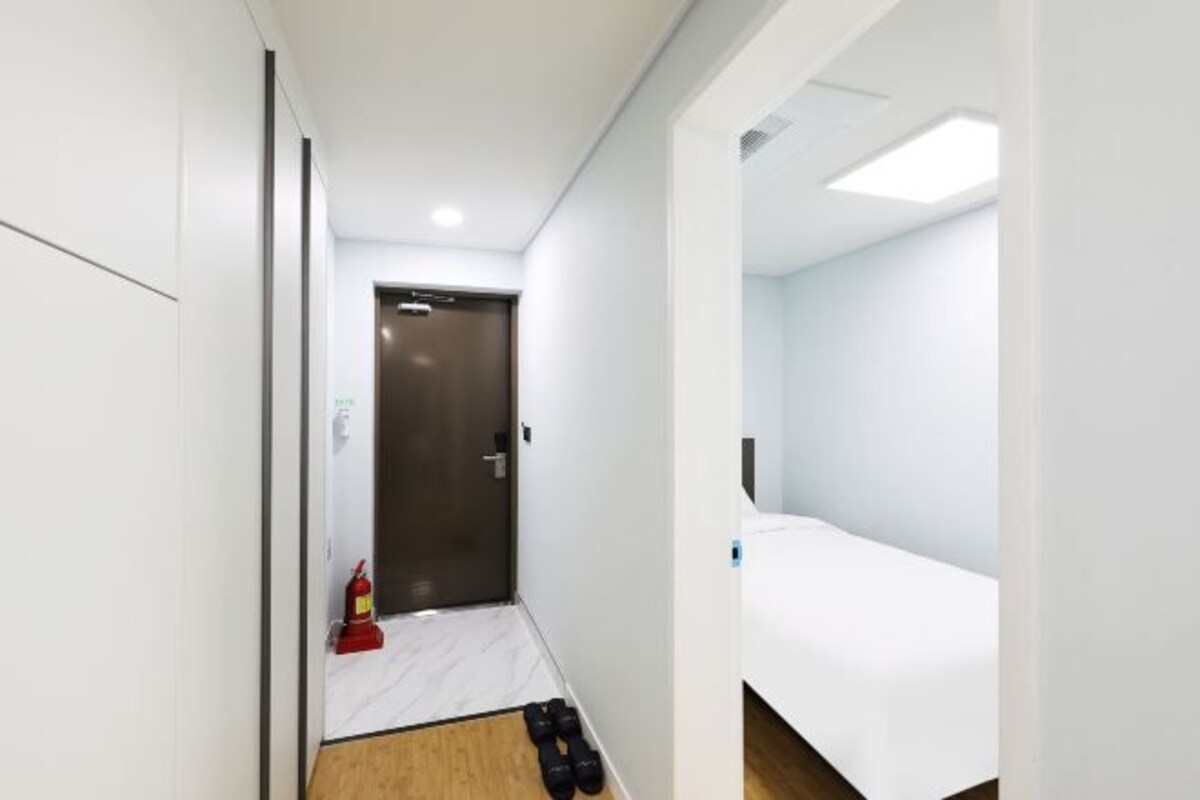 Une chambre d’hôtel avec un lit, une porte et un petit couloir où se trouvent un extincteur et des chaussures.