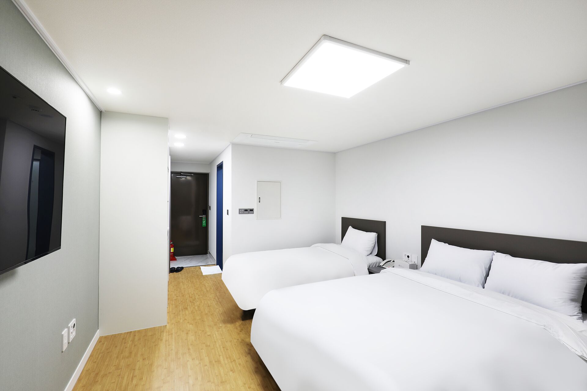Habitación de hotel con dos camas, un televisor de pantalla plana, una puerta y una lámpara en el techo.