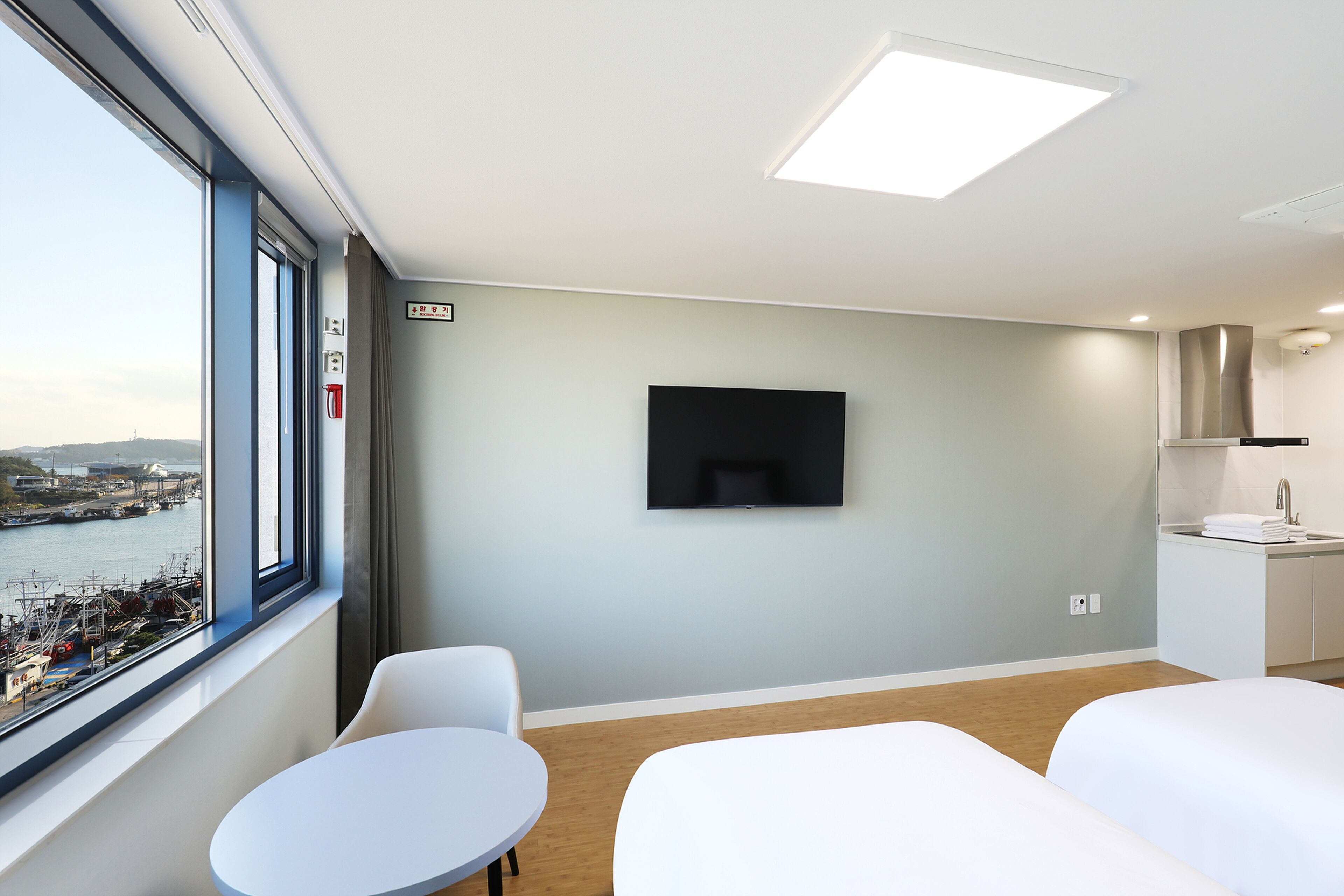 A modern hotel room with a large window, a flat-screen TV, a small round table, and a bed.