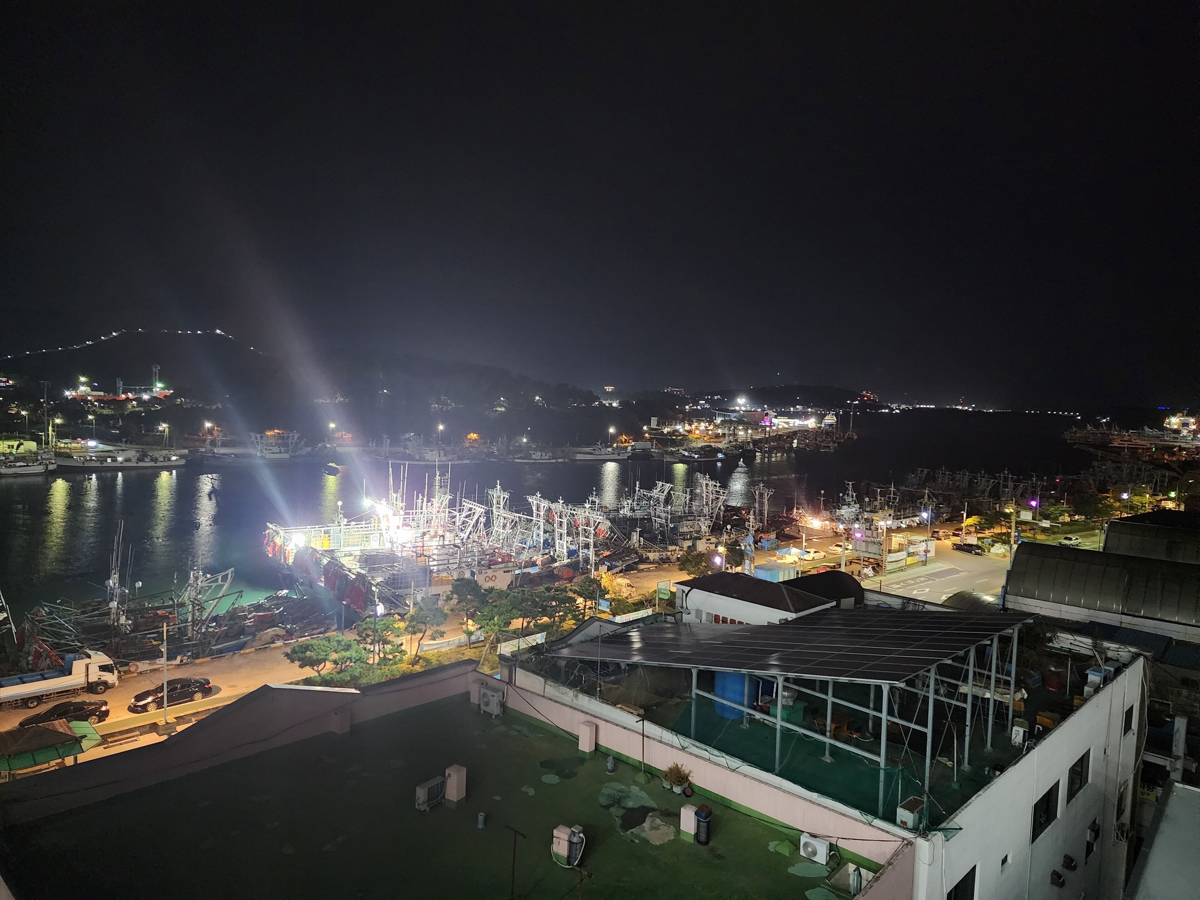 A nighttime view of a harbor with boats, a dock, and buildings with lights.